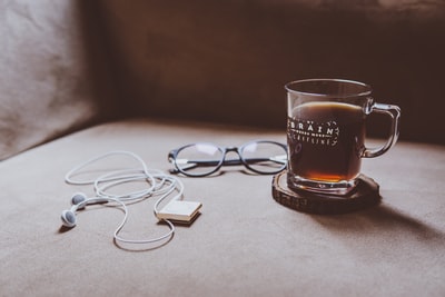 棕色木板杯垫上印有清晰大脑图案的玻璃杯，旁边是黑框眼镜和白色耳机